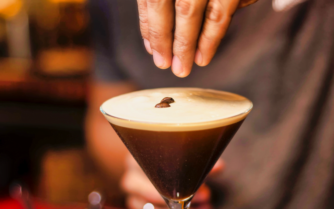 A glass of Espresso Martini being garnished with whole coffee beans.