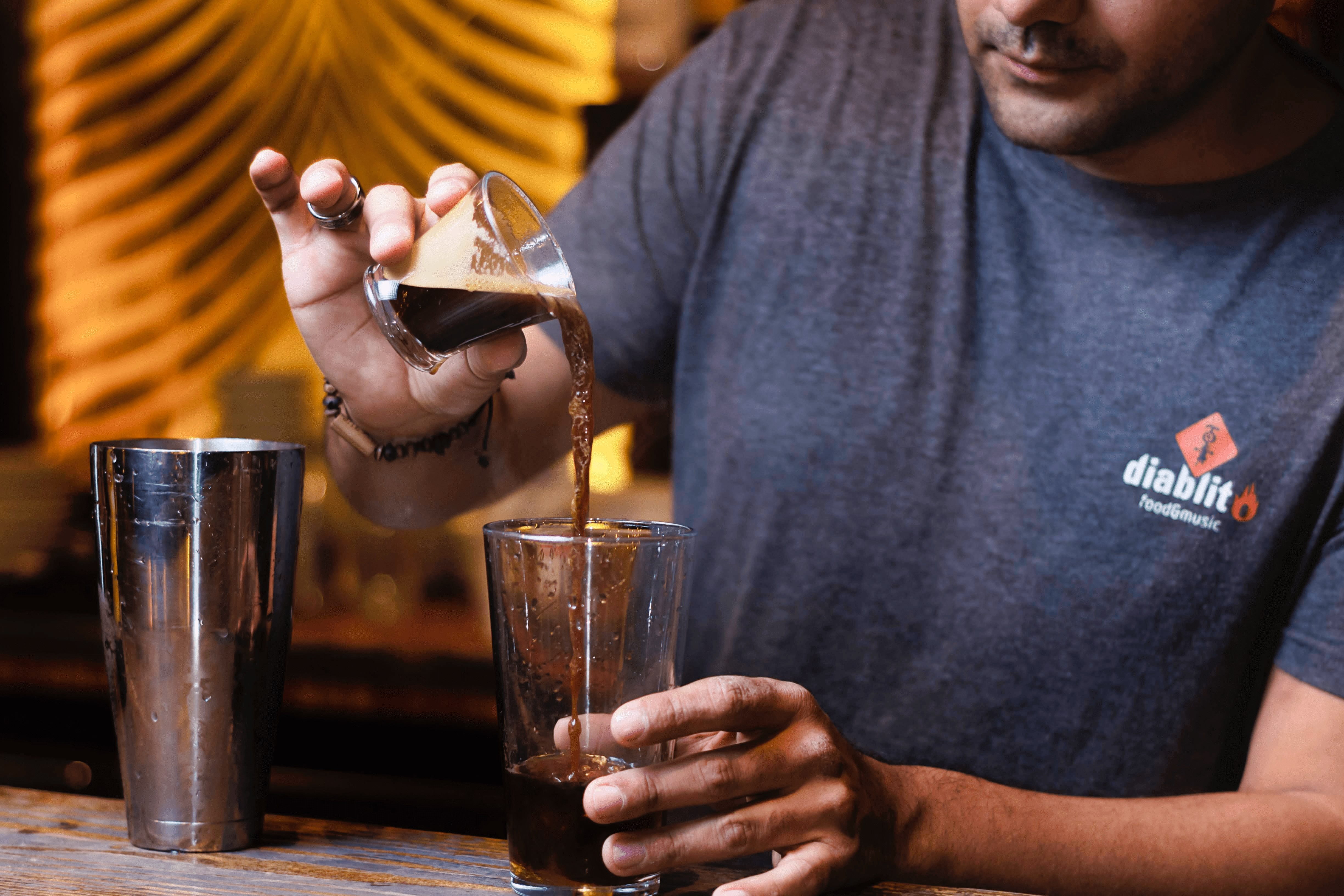A shot of espresso being poured into a stirring glass by a bartender.