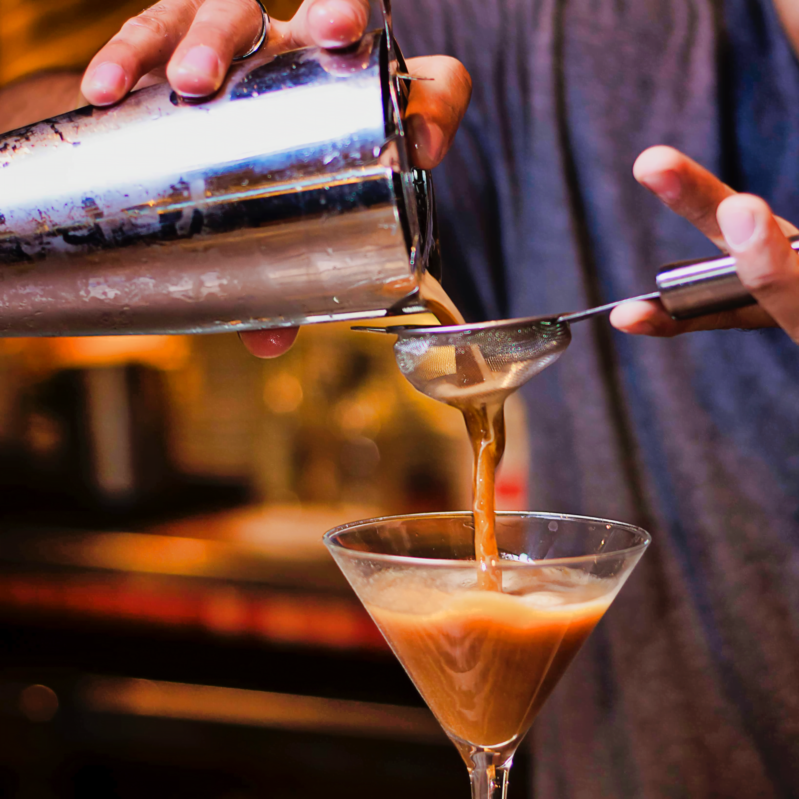 An Espresso Martini being strained our of a shaker cup and into a martini glass.